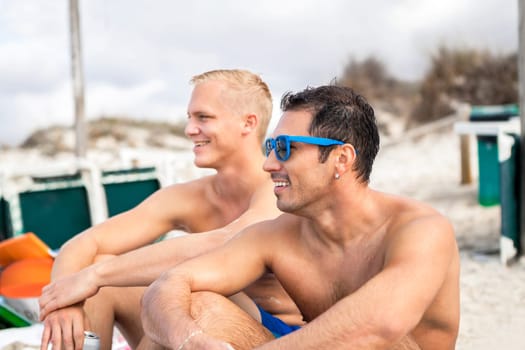 Two young men friends relax in the sand while on holiday on the beach in summer