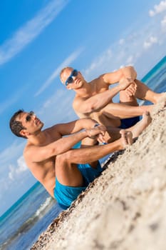 Two young men friends relax in the sand while on holiday on the beach in summer