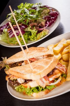 Club sandwich on toasted white bread with bacon and fries fried fries on a plate