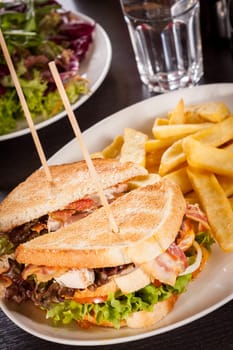 Club sandwich on toasted white bread with bacon and fries fried fries on a plate