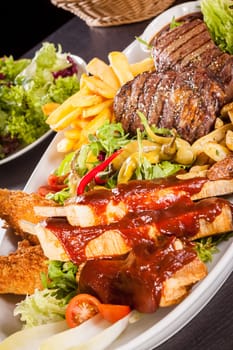 Huge barbecue plate with mixed meat and steaks on salad