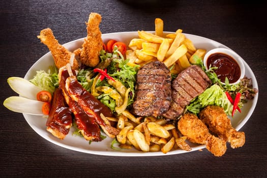 Huge barbecue plate with mixed meat and steaks on salad