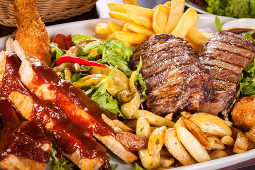 Huge barbecue plate with mixed meat and steaks on salad
