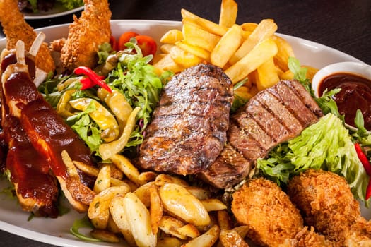 Huge barbecue plate with mixed meat and steaks on salad