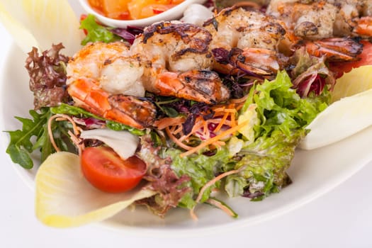 Roasted shrimp on a skewer on mixed salad with dip and foil potato prepared on a plate insulated against a white background