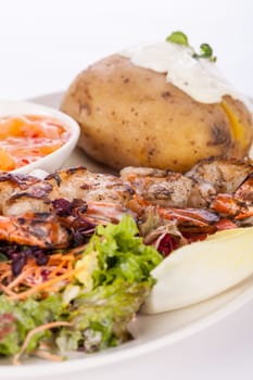 Roasted shrimp on a skewer on mixed salad with dip and foil potato prepared on a plate insulated against a white background