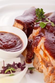 Grilled pork ribs Spareribs with barbecue sauce marinade and herb salad on a plate isolated against a white background