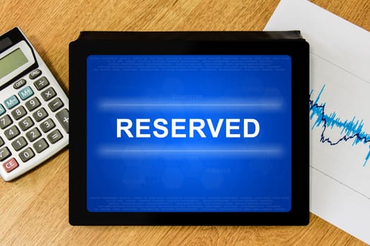 reserved word on digital tablet with calculator and financial graph