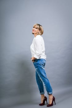 adult blonde attractive woman with blue jeans and white blouse against grey background fashion trendy