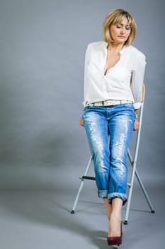 adult blonde attractive woman with blue jeans and white blouse against grey background fashion trendy