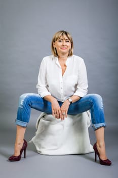 adult blonde attractive woman with blue jeans and white blouse against grey background fashion trendy