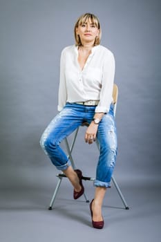 adult blonde attractive woman with blue jeans and white blouse against grey background fashion trendy