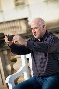 Attractive older man senior photographs himself with his mobile phone smartphone in the park