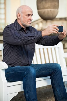 Attractive older man senior photographs himself with his mobile phone smartphone in the park