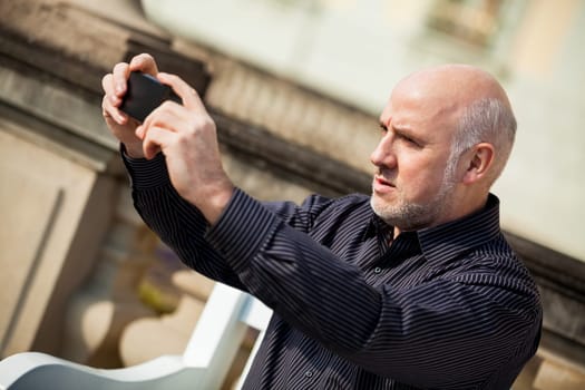 Attractive older man senior photographs himself with his mobile phone smartphone in the park