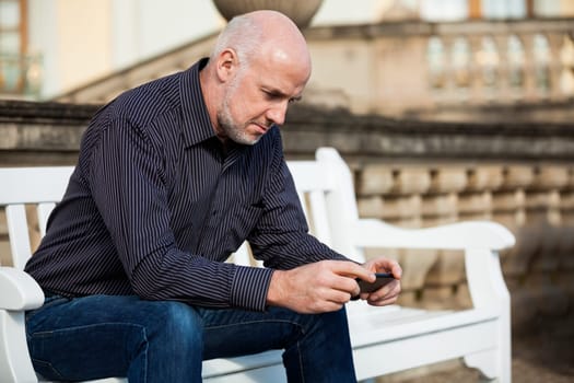 Attractive older man senior with mobile phone smartphone on a bench in the park in summer