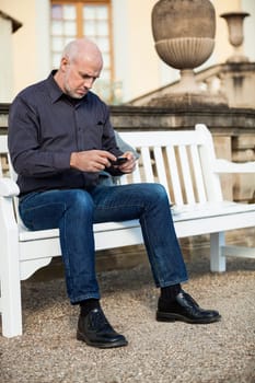 Attractive older man senior with mobile phone smartphone on a bench in the park in summer