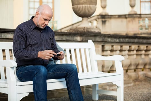 Attractive older man senior with mobile phone smartphone on a bench in the park in summer