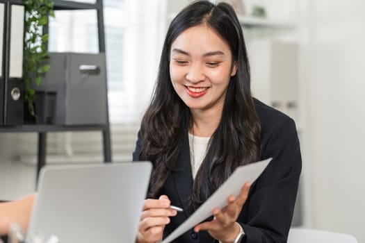 A confident businesswoman smiles while reviewing documents and collaborating with a colleague in a contemporary office environment.