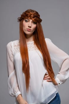 Young attractive female girl with long red hair in portrait against grey background