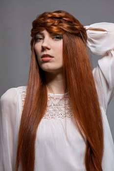 Young attractive female girl with long red hair in portrait against grey background