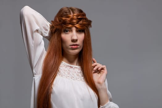 Young attractive female girl with long red hair in portrait against grey background
