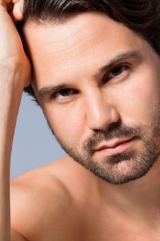 Young naked man with dark hair and beard as a portrait against a grey background