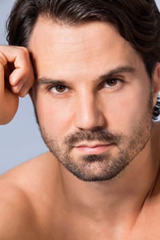 Young naked man with dark hair and beard as a portrait against a grey background