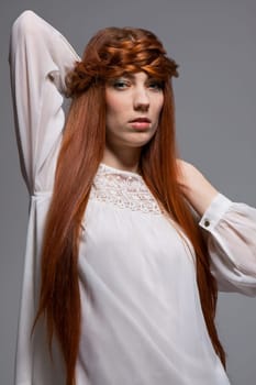 Young attractive female girl with long red hair in portrait against grey background