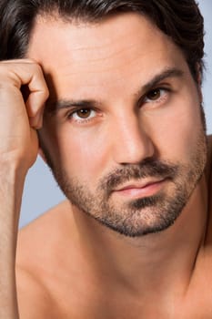 Young naked man with dark hair and beard as a portrait against a grey background