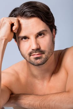 Young naked man with dark hair and beard as a portrait against a grey background