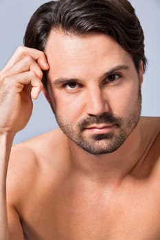 Young naked man with dark hair and beard as a portrait against a grey background