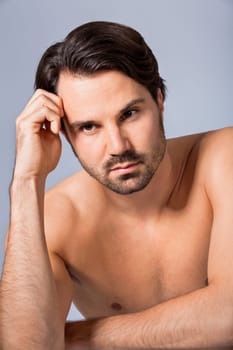 Young naked man with dark hair and beard as a portrait against a grey background