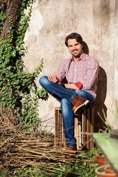 Young man with a plaid shirt and jeans with dark hair and beard outdoors under an efeuranke in daylight