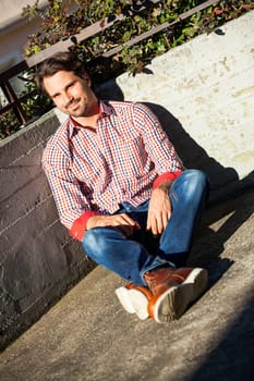 Young man with a checked shirt sits on a wall in the sun and relaxes