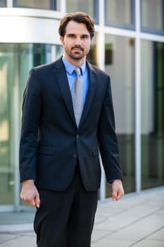 Young trendy businessman in front of a business building successfully with beard and dark hair