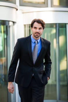 Young trendy businessman in front of a business building successfully with beard and dark hair