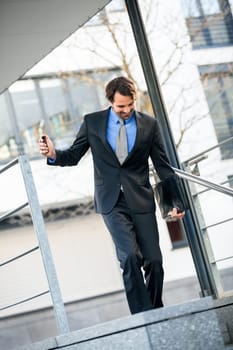 Cheerful successful businessman with dark suit and dark hair joyfully in front of a commercial building