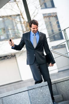 Cheerful successful businessman with dark suit and dark hair joyfully in front of a commercial building