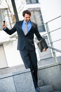 Cheerful successful businessman with dark suit and dark hair joyfully in front of a commercial building