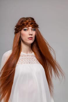 Young attractive female girl with long red hair in portrait against grey background