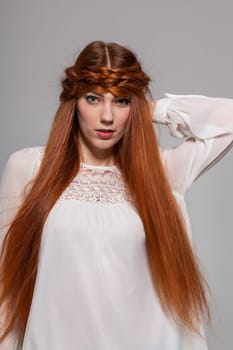 Young attractive female girl with long red hair in portrait against grey background
