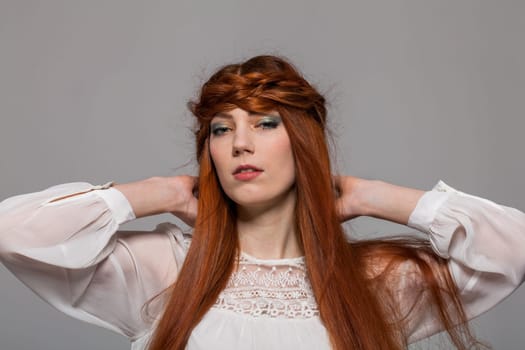 Young attractive female girl with long red hair in portrait against grey background