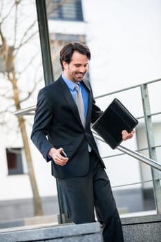 Cheerful successful businessman with dark suit and dark hair joyfully in front of a commercial building