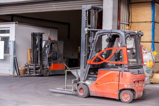 Small orange forklift in front of a warehouse with freight traffic and goods in the background