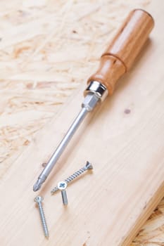 Close-up of a cross screwdriver with screws in wood while DIY in a workshop