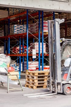 Small orange forklift in front of a warehouse with many pallets in daylight