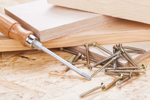 Close-up of a cross screwdriver with screws in wood while DIY in a workshop