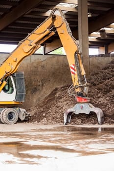 Excavator with gripper arm in front of a large pile of brown earth in the construction industry