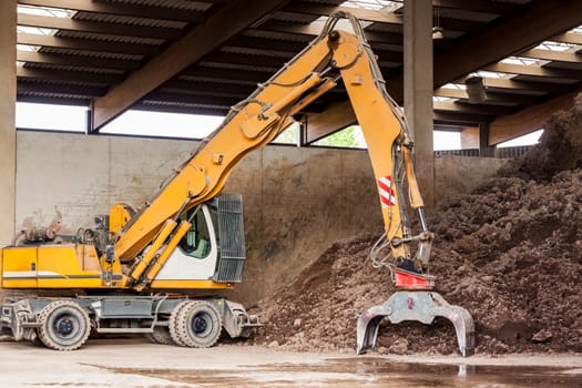 Excavator with gripper arm in front of a large pile of brown earth in the construction industry